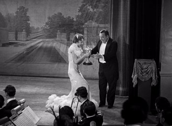 Movie still from “San Francisco” (1936), directed by W.S. Van Dyke – A man and a woman holding a trophy on a stage; Medium shot, Over the shoulder angle