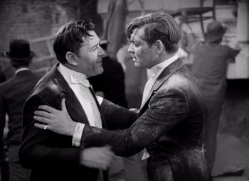 Movie still from “San Francisco” (1936), directed by W.S. Van Dyke – A black - and - white photo of two men hugging; Medium shot, High angle
