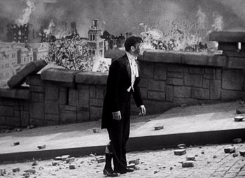 Movie still from “San Francisco” (1936), directed by W.S. Van Dyke – A black and white photo of a man walking in front of a wall of fire; Wide shot, Low angle