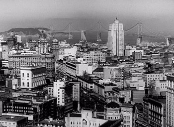 Movie still from “San Francisco” (1936), directed by W.S. Van Dyke – A black and white photo of a city with a bridge in the background; Extreme Wide shot, High angle