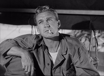 Movie still from “Sands of Iwo Jima” (1949), directed by Allan Dwan – A man smoking a cigarette while sitting on top of a bench; Close Up shot, Low angle