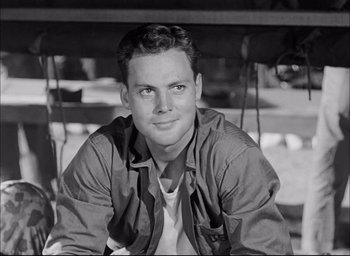 Movie still from “Sands of Iwo Jima” (1949), directed by Allan Dwan – Black and white photograph of a young man sitting in front of a bench; Close Up shot, Low angle
