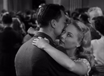 Movie still from “Sands of Iwo Jima” (1949), directed by Allan Dwan – A man and a woman hugging each other in front of a crowd of onlookers; Close Up shot, Over the shoulder angle