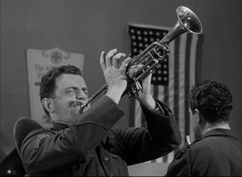 Movie still from “Sands of Iwo Jima” (1949), directed by Allan Dwan – A man playing a trumpet in front of an american flag; Medium shot, Low angle