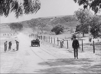 Movie still from “Sands of Iwo Jima” (1949), directed by Allan Dwan – A black and white photo of a car driving down a dirt road; Extreme Wide shot, High angle