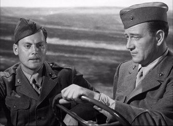 Movie still from “Sands of Iwo Jima” (1949), directed by Allan Dwan – Two men in military uniforms looking at each other while holding a steering wheel; Medium shot, Over the shoulder angle