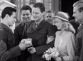 Movie still from “Sands of Iwo Jima” (1949), directed by Allan Dwan – A group of people standing around each other holding a gift; Medium shot, Over the shoulder angle