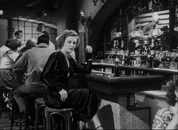 Movie still from “Sands of Iwo Jima” (1949), directed by Allan Dwan – A woman sitting at a bar drinking a beer; Medium shot, Low angle