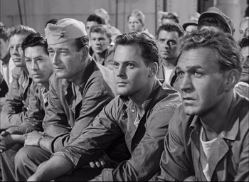 Movie still from “Sands of Iwo Jima” (1949), directed by Allan Dwan – A black and white photo of a group of men sitting together; Medium shot, High angle