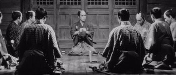 Movie still from “Sanjuro” (1962), directed by Akira Kurosawa – A man sitting on the ground in front of three other men; Medium shot, High angle