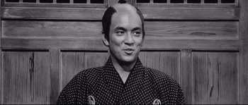 Movie still from “Sanjuro” (1962), directed by Akira Kurosawa – A black and white photo of a man with a shaved head; Close Up shot, Low angle
