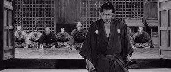 Movie still from “Sanjuro” (1962), directed by Akira Kurosawa – A man in a robe standing in front of two other men; Medium shot, Low angle