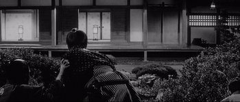 Movie still from “Sanjuro” (1962), directed by Akira Kurosawa – A woman sitting on the ground in front of a building; Wide shot, Low angle