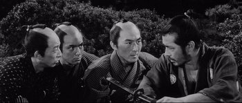 Movie still from “Sanjuro” (1962), directed by Akira Kurosawa – A group of men sitting next to each other in front of a bush; Close Up shot, High angle