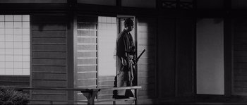 Movie still from “Sanjuro” (1962), directed by Akira Kurosawa – A man holding a baseball bat while standing next to a window; Wide shot, Low angle