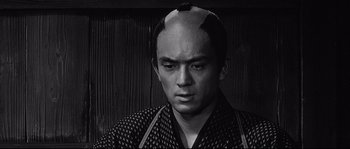 Movie still from “Sanjuro” (1962), directed by Akira Kurosawa – A black and white photo of a man with a shaved head; Close Up shot, Over the shoulder angle