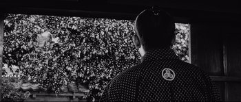 Movie still from “Sanjuro” (1962), directed by Akira Kurosawa – A man standing in front of a crowd of people; Medium shot, Over the shoulder angle