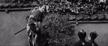 Movie still from “Sanjuro” (1962), directed by Akira Kurosawa – A black and white photo of a man holding a plant; Medium shot, High angle