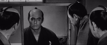 Movie still from “Sanjuro” (1962), directed by Akira Kurosawa – A black and white photo of a man with a bald head; Close Up shot, Over the shoulder angle