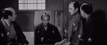 Movie still from “Sanjuro” (1962), directed by Akira Kurosawa – A man with a shaved head is holding a sword in front of another man with a shaved head; Medium shot, Over the shoulder angle