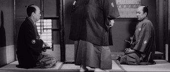 Movie still from “Sanjuro” (1962), directed by Akira Kurosawa – A person standing in front of a wall wearing a robe; Medium shot, Low angle