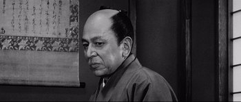 Movie still from “Sanjuro” (1962), directed by Akira Kurosawa – An older man with a shaved head is looking to his left; Close Up shot, Low angle