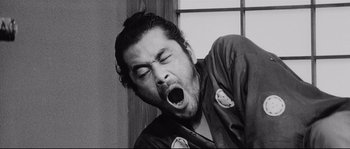 Movie still from “Sanjuro” (1962), directed by Akira Kurosawa – A black and white photo of a man with his mouth wide open; Medium shot, Low angle