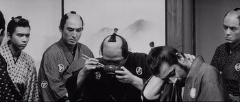 Movie still from “Sanjuro” (1962), directed by Akira Kurosawa – A man with two other people holding chopsticks and eating food; Close Up shot, Over the shoulder angle