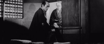 Movie still from “Sanjuro” (1962), directed by Akira Kurosawa – A man in a black kimono is looking at himself in a mirror; Medium shot, Low angle