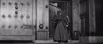Movie still from “Sanjuro” (1962), directed by Akira Kurosawa – A man in a robe is standing in front of a door; Wide shot, Low angle