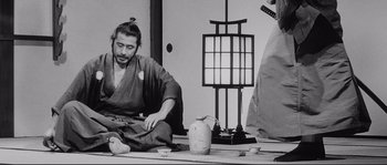 Movie still from “Sanjuro” (1962), directed by Akira Kurosawa – A man sitting on the ground in front of a lamp; Medium shot, Low angle