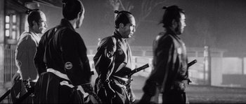 Movie still from “Sanjuro” (1962), directed by Akira Kurosawa – A black and white photo of a man in samurai garb; Medium shot, Low angle