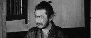 Movie still from “Sanjuro” (1962), directed by Akira Kurosawa – A man with long black hair wearing a black shirt; Close Up shot, Low angle