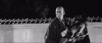 Movie still from “Sanjuro” (1962), directed by Akira Kurosawa – A black and white photo of a man in a kimono; Medium shot, Low angle