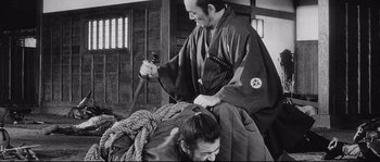 Movie still from “Sanjuro” (1962), directed by Akira Kurosawa – A man in a kimono holds a sword over a woman's head; Medium shot, Over the shoulder angle