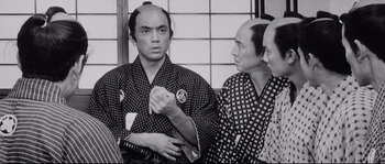 Movie still from “Sanjuro” (1962), directed by Akira Kurosawa – A man in a black and white photo with two other men; Close Up shot, Over the shoulder angle