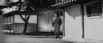Movie still from “Sanjuro” (1962), directed by Akira Kurosawa – A man standing in front of a building in an old photo; Wide shot, Low angle