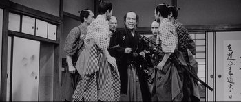 Movie still from “Sanjuro” (1962), directed by Akira Kurosawa – A group of men standing next to each other holding swords; Medium shot, Over the shoulder angle
