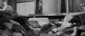 Movie still from “Sanjuro” (1962), directed by Akira Kurosawa – A black - and - white photo of a person sitting on a bench; Wide shot, Low angle