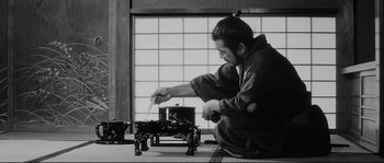 Movie still from “Sanjuro” (1962), directed by Akira Kurosawa – A man in traditional japanese garb cooking food on an outdoor stove; Medium shot, Low angle
