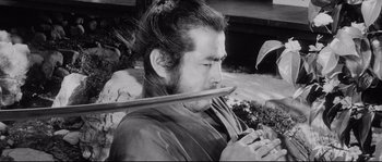 Movie still from “Sanjuro” (1962), directed by Akira Kurosawa – A man holding a long wooden stick in his mouth; Medium shot, Low angle