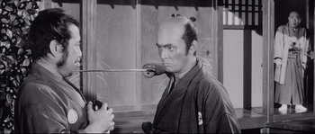 Movie still from “Sanjuro” (1962), directed by Akira Kurosawa – An old photo of a man with a sword in his mouth; Medium shot, Over the shoulder angle