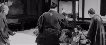 Movie still from “Sanjuro” (1962), directed by Akira Kurosawa – A man in a robe is holding a stick; Medium shot, Over the shoulder angle