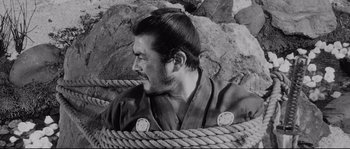 Movie still from “Sanjuro” (1962), directed by Akira Kurosawa – A black and white photo of a man with a rope around his neck; Close Up shot, High angle