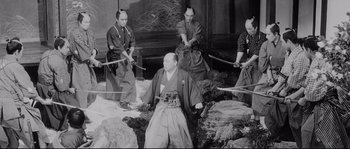 Movie still from “Sanjuro” (1962), directed by Akira Kurosawa – A group of men in traditional japanese garb holding swords; Wide shot, Over the shoulder angle