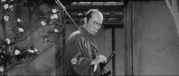 Movie still from “Sanjuro” (1962), directed by Akira Kurosawa – A man holding a samurai sword in his hands; Medium shot, Over the shoulder angle