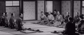 Movie still from “Sanjuro” (1962), directed by Akira Kurosawa – A black and white photo of a group of men sitting on the ground; Wide shot, High angle