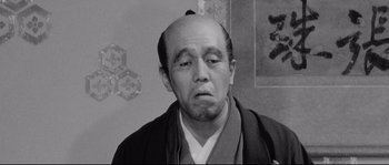 Movie still from “Sanjuro” (1962), directed by Akira Kurosawa – An older man in a traditional japanese garb looking sad; Close Up shot, Low angle