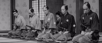 Movie still from “Sanjuro” (1962), directed by Akira Kurosawa – A group of men sitting on the ground in front of a window; Medium shot, Low angle
