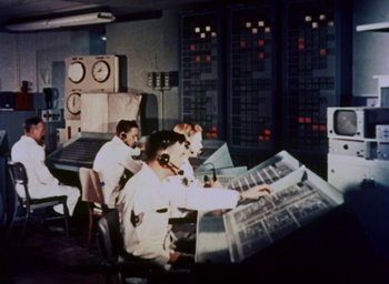 Movie still from “Santa Claus Conquers the Martians” (1964), directed by Nicholas Webster – A group of men working in a room with computers on the wall; Wide shot, Low angle